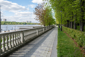 Scenic Riverside Walkway With Lush Greenery and Clear Sky in a City Park During a Sunny Afternoon
