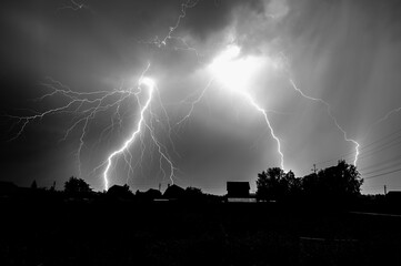 Multiple lightning bolts are illuminating the dark sky over a residential area during a powerful thunderstorm