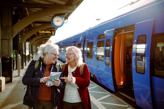 Senior women using map at train station while traveling together