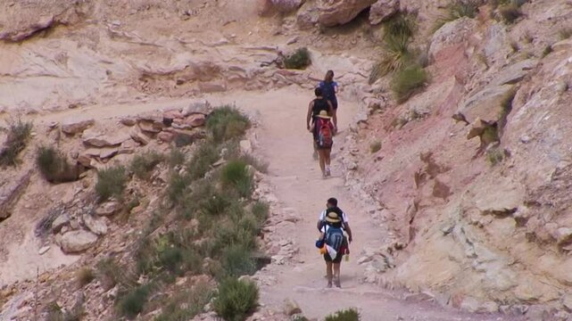 Tele to wide pan of hikers descending into Hualapai canyon on the way to Supai Village by way of the Havasupai Trail near Arizona's Grand Canyon.  A steep redrock canyon is revealed.
