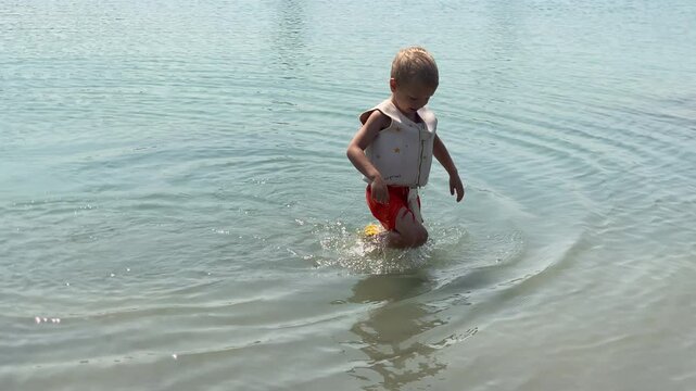 A child is captured mid-movement, creating ripples as they wade through the shallow, light blue water of a lake near Simferopol, Crimea. The scene conveys a sense of playful enjoyment and refreshment