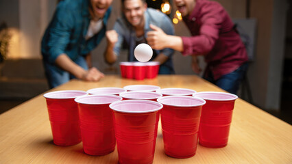 Group of friends playing beer pong with red cups at party, fun and competitive drinking game for International Beer Day