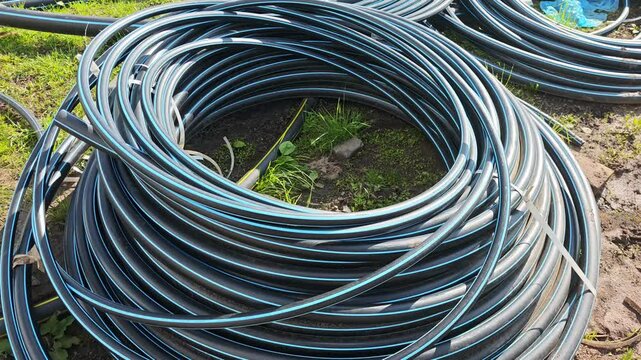 Multiple coils of black polyethylene pipes lay on the ground, prepared for agricultural irrigation or other water management purposes