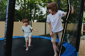 Active boys playing on a trampoline, enjoying a sunny day with laughter and excitement in a vibrant...