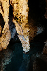 Unique rock formation suspended over blue water inside illuminated section of Stopica Cave. Zlatibor, Serbia country. A popular place among tourists in low season