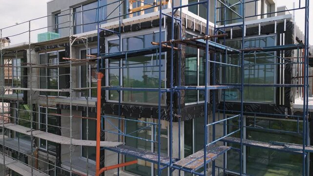 video of a modern building under construction with blue scaffolding. Exterior finishing work in progress, featuring concrete walls and large glass windows