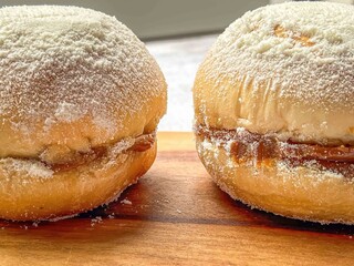 Close up of two sonhos filled with cream and topped with powdered sugar on a wooden surface
