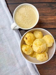 A top view of cheese bread in a bowl with a cup of coffee placed on a wooden table with a cloth