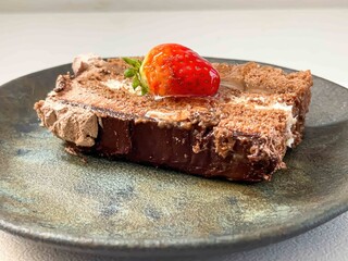 A slice of chocolate cake with strawberry on top served on a ceramic plate on a white background