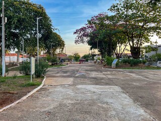 Obraz premium View of a concrete park pathway with trees and benches under a blue and yellow sky at sunset time
