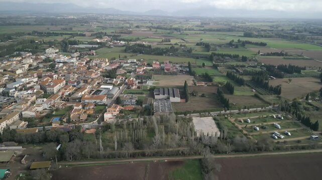 Vista a&eacute;rea de un pueblo de Girona con casas tradicionales, rodeado de naturaleza y una gran &aacute;rea de autocaravanas.