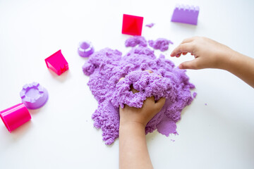 Child playing with purple kinetic sand and plastic toy shapes on white background