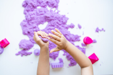 Child hands playing with purple kinetic sand and molds on white background