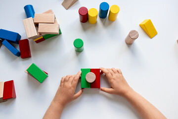 Child hands playing with colorful wooden blocks on white surface