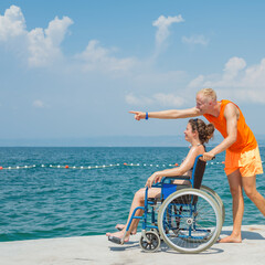 Smiling woman with a disability and her assistant helping her wheelchair move, enjoying time at the...