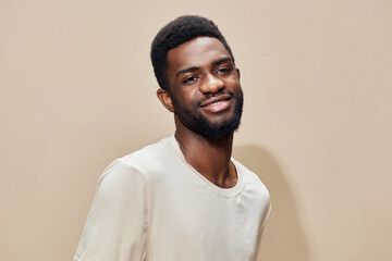 Smiling young African man in casual beige shirt against a light neutral background, showcasing...