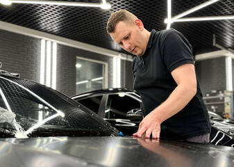 A car wrapping specialist applies a polyurethane film to the car. Detailer smoothes PPF. Car wrapping, detailing, tuning and styling. Selective focus. PPF protective film against chips and scratches. 