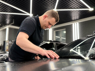 A car wrapping specialist applies a polyurethane film to the car. Detailer smoothes PPF. Car wrapping, detailing, tuning and styling. Selective focus. PPF protective film against chips and scratches. 