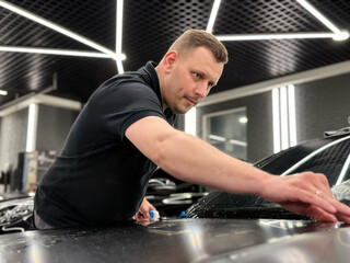 A car wrapping specialist applies a polyurethane film to the car. Detailer smoothes PPF. Car wrapping, detailing, tuning and styling. Selective focus. PPF protective film against chips and scratches. 