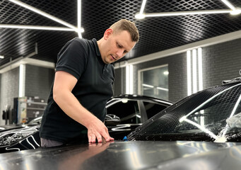 A car wrapping specialist applies a polyurethane film to the car. Detailer smoothes PPF. Car wrapping, detailing, tuning and styling. Selective focus. PPF protective film against chips and scratches. 