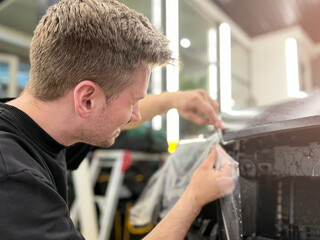 A car wrapping specialist applies a polyurethane film to the car. Detailer smoothes PPF. Car...