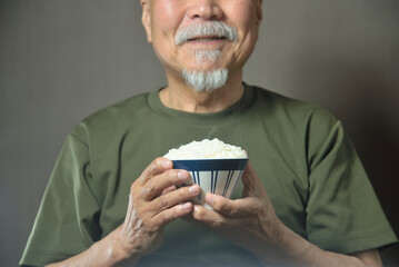 お茶碗で湯気の立ちのぽる温かいご飯を食べる老人
