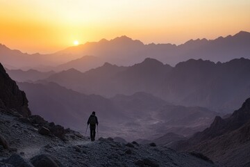 Fototapeta premium Lone hiker silhouetted against a stunning mountain range at sunset, creating a breathtaking vista of color and depth in nature.