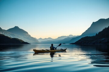 A lone kayaker paddles through serene waters at sunset, surrounded by majestic mountains under a clear sky.