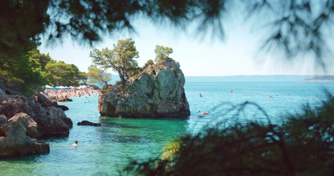 Crowded Brela beach with swimmers near rocky island and clear sea water in Croatia