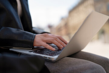 Person working on laptop outside in urban setting during daylight, focused on task while enjoying...