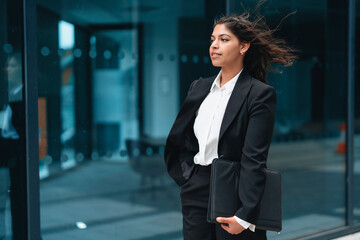 Professional woman in sleek business attire standing confidently outside modern office building...