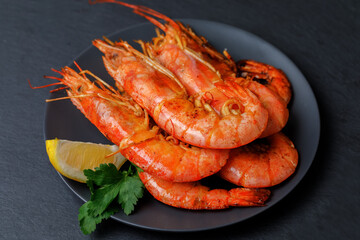 Fried shrimps on a plate with piece of lemon on black background. Top view, copy space.