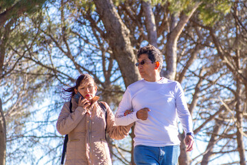 Couple enjoying a sunny stroll under trees in a peaceful park during a winter day