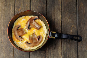 Omelet with mushrooms and pieces of bread in a pan on wooden background. Rustic nutrition breakfast. Side view.