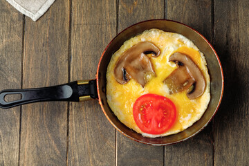 Omelet with mushrooms and tomato in a pan on wooden background. Rustic nutrition breakfast. Top...