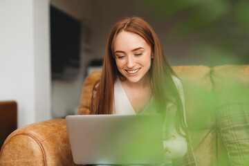 Young woman enjoying leisure time while using a laptop on a comfortable couch in a cozy indoor space during the day