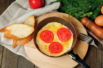 Omelet with tomatoes and pieces of bread in a pan on wooden background. Rustic nutrition breakfast. Top view.