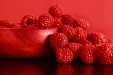 Raspberries in a red wooden bowl against a red background backdrop.