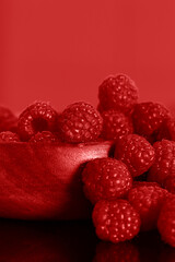 Raspberries in a red wooden bowl against a red background backdrop.