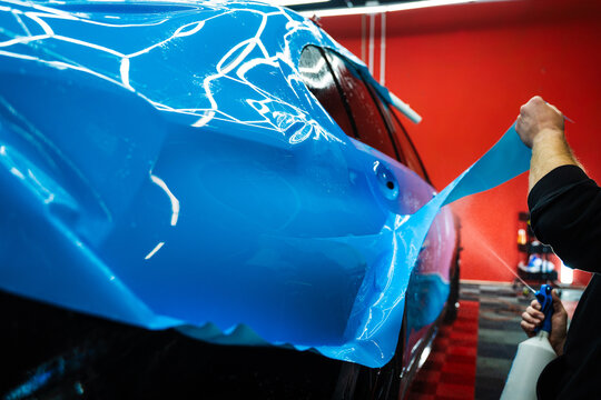 Detailing experts use hydration spray for controlled application of blue PPF film. Detailer uses spray-assisted method to apply vibrant blue vinyl wrap for perfect, bubble-free alignment.