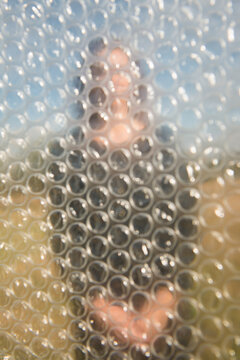 conceptual abstract outdoor art portrait of woman in black dress behind transparant plastic bubble foil sheet
