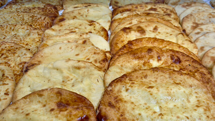 Traditional Georgian khachapuri flatbreads arranged in rows, golden baked crusts with visible cheese filling, showcasing variety and texture of regional baked goods, food concept