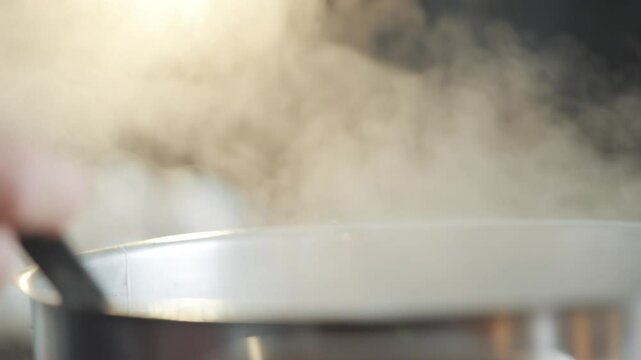 A hand is stirring a pot of food. The pot is filled with a thick, bubbling liquid. The steam rising from the pot creates a cozy, homey atmosphere