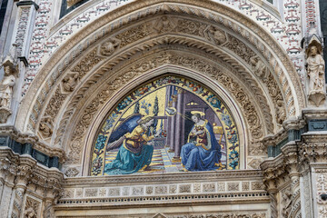 Mosaic of the Annunciation above a side entrance of Florence Cathedral, Tuscany, Italy. Detailed religious artwork framed by ornate gothic carvings