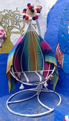 An egg shaped chair, decorated with a colorful Moroccan blanket and striped pillow, sits in a corner, surrounded by cheerful artistic murals in bright blue and white colors.