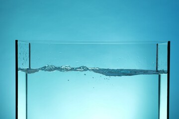 Glass aquarium with splashing water on light blue background, closeup