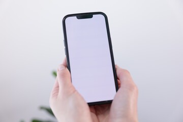 Woman holding smartphone with blank screen on blurred background, closeup. Mockup for design