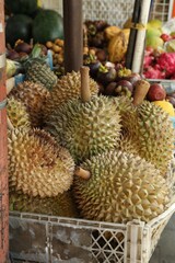 Fresh ripe durians in crate and other different fruits at market, closeup