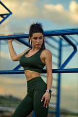 sporty girl confidently poses near exercise equipment on sports ground overlooking the sea at sunset vibrant sky complements her energetic stance and athletic outfit