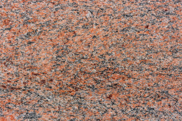 View of red granite surface, showcasing its rough, natural texture. The stone is speckled with black, grey, and white mineral grains, creating a captivating and irregular pattern.